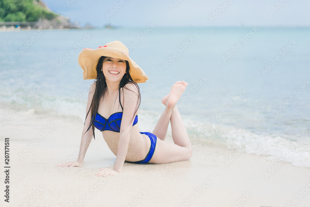Pretty beautiful asian woman wearing colourful swimwear bikini with hat living sunbathing on the beach in the summer