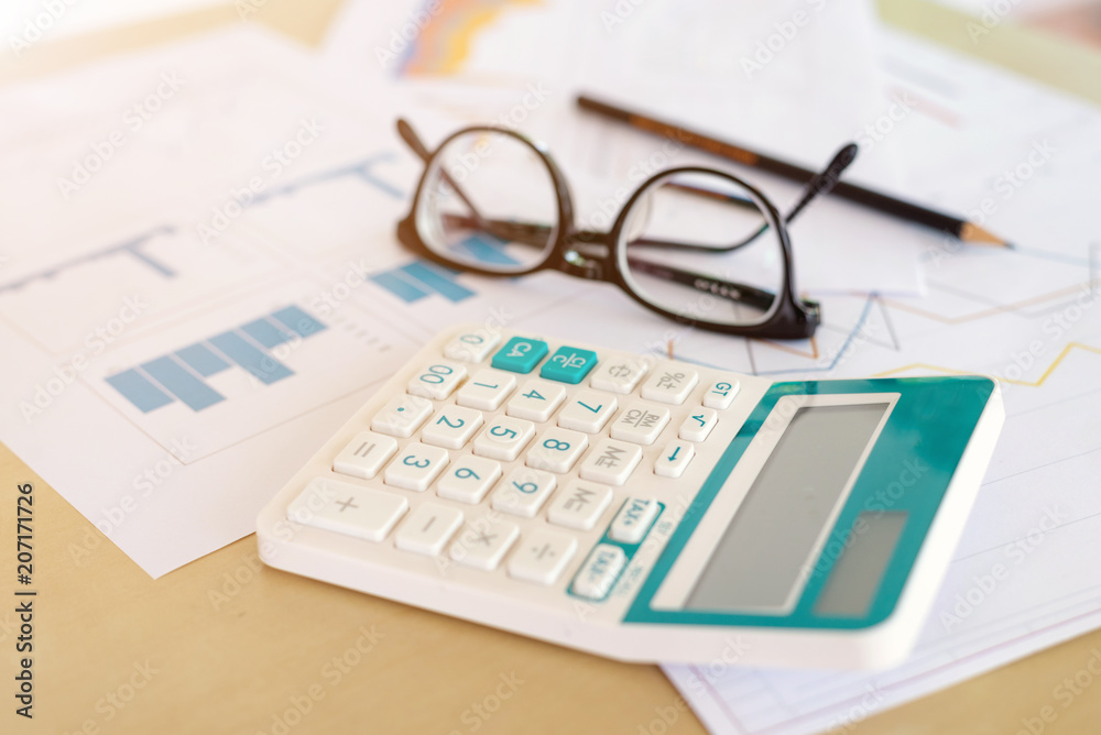 business office desk workplace with calculator, graph report, eyeglasses and pencil on wooden table business office desk workplace with calculator, graph report, eyeglasses and pencil on wooden table