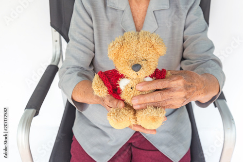 senior woman sitting on chair and holding teddy bear