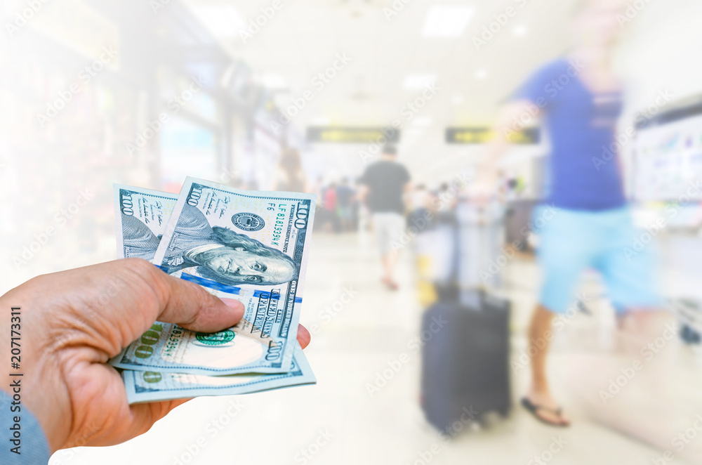 Business woman hand holding American dollar Currency isolated on blurred background travelers walking with a luggage at airport terminal, travel cost concept