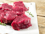 Pieces of raw meat. Raw beef with spices on white parchment paper on wooden rough rustic background, side view, close-up