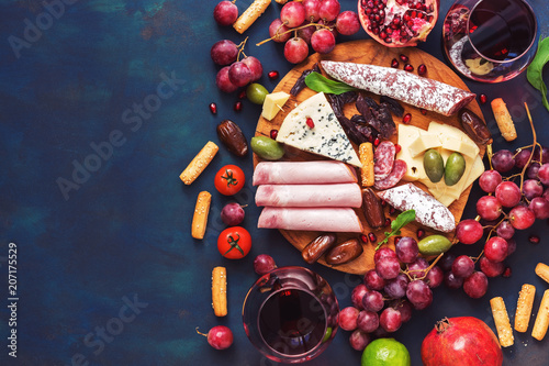 Various appetizer-red wine, fruits,sausages,cheese, vegetables on a dark finem background. Copy space, top view.