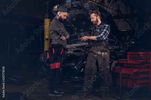 Two mechanics talking during repairs a broken car in a garage.