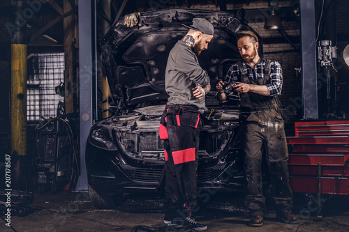 Two mechanics talking during repairs a broken car in a garage.