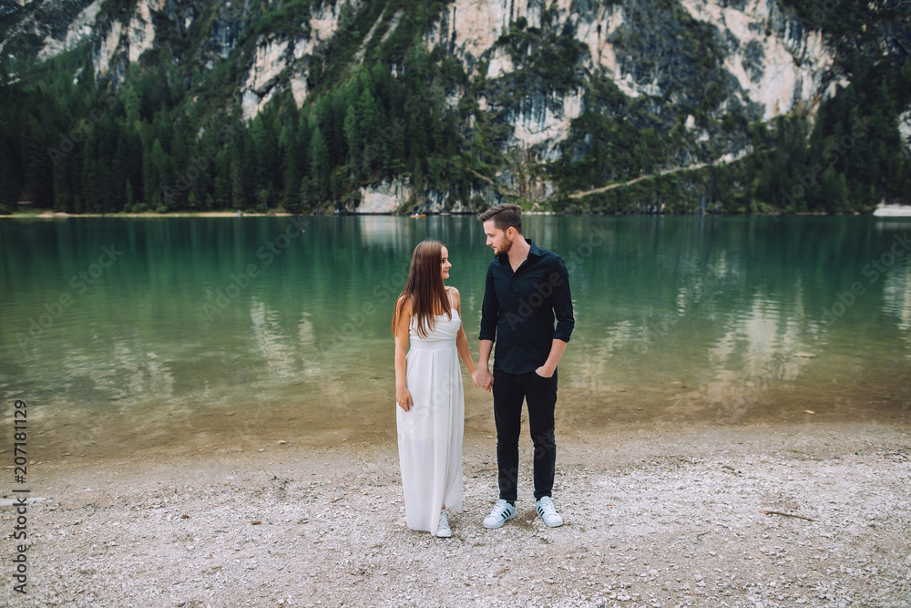 Young couple sitting next to a young couple sitting next to a beautiful lake in the alpine mountains. young people are dressed in beautiful clothes. The old woman is dressed in a white dress