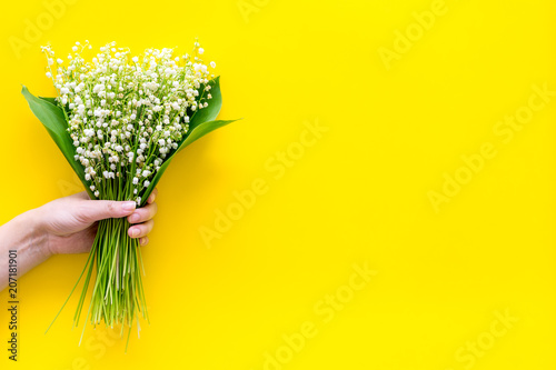 Give a bouquet of delicate lily of the valley flowers. Hand hold bunch of flowers on yellow background top view copy space