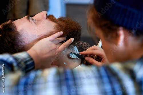 Close up of a hairdresses work for an attractive young blond man at the barber shop. He is doing styling of his beard, shaving with straight razor photo