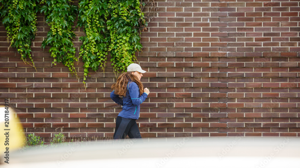 Young woman jogging along the street in eurpean city in the morning. Running fitness girl against brick wall Young woman jogging along the street in eurpean city in the morning. Running fitness girl against brick wall