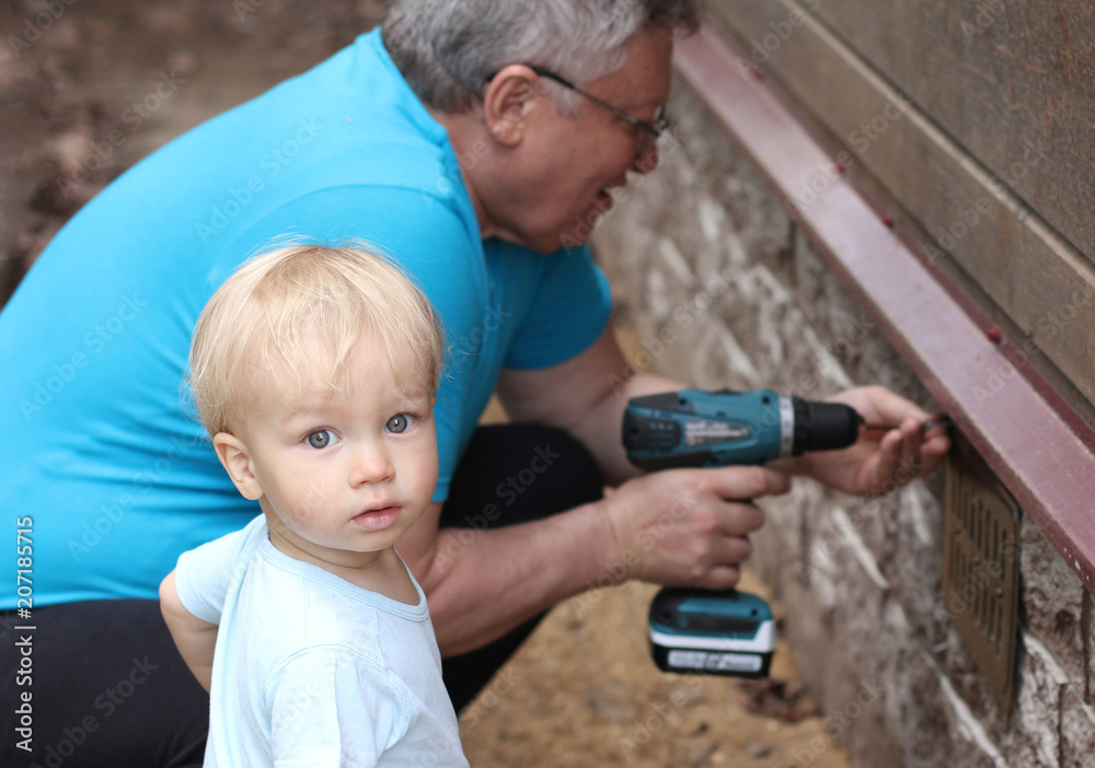 Little baby grandson and his grandfather works with screwdriver (fastens the ventilation grille). Little baby grandson and his grandfather works with screwdriver (fastens the ventilation grille).
