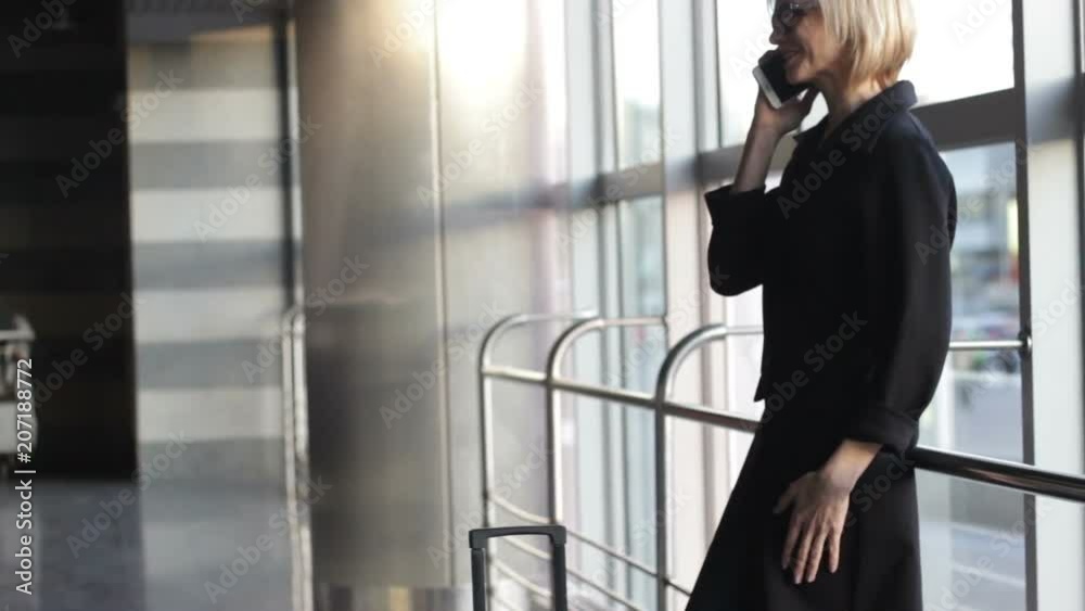 Happy passenger wearing black dress, waiting train, talking over phone, smiling Happy passenger wearing black dress, waiting train, talking over phone, smiling
