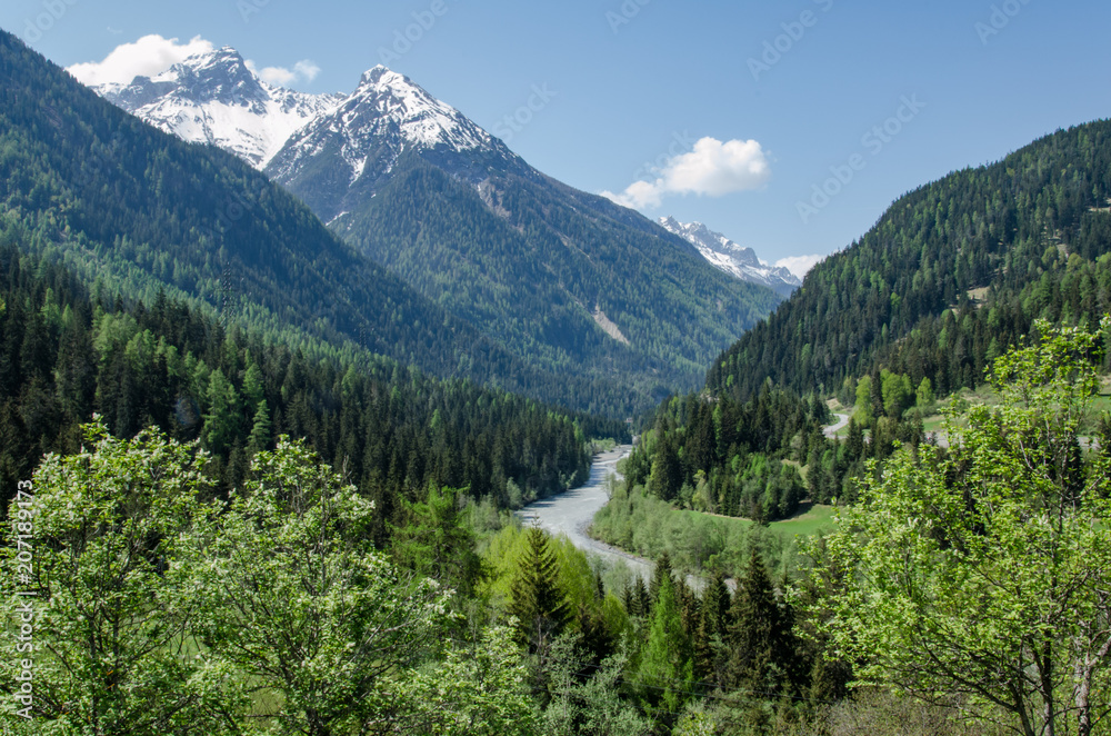 View of Inn river in (Engadin) Switzerland with mountain in background on warm spring day with green trees