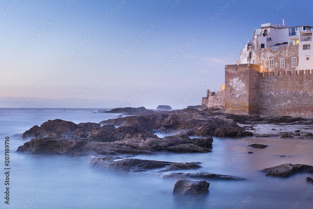 rocks in water and city walls after sunset time in Morocco
