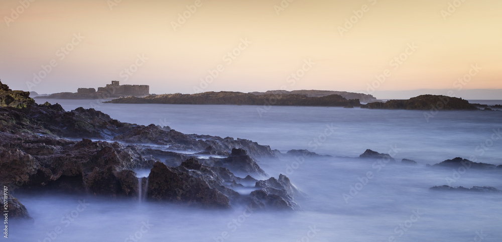 blue water and orange sky above ruins of old fort in Morocco