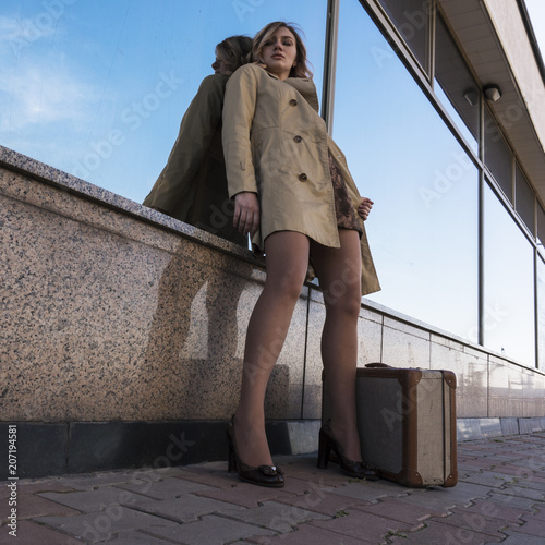 Attractive Young Blonde Woman in Trench walking in City with Vintage Suitcase photo