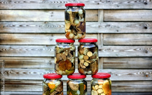 Delicious food, kitchen and homemade concept: forest mushrooms in jars on a wooden background.