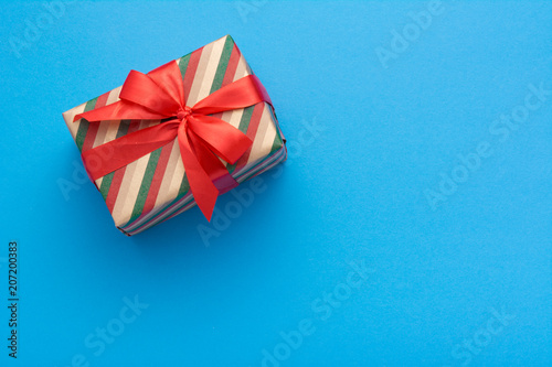 Hands holding wrapped gift box with colored ribbon as a present for Christmas, new year, mother's day, anniversary, birthday, party,  on blue background, top view. Present for a colleague at work.