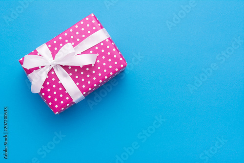 Hands holding wrapped gift box with colored ribbon as a present for Christmas, new year, mother's day, anniversary, birthday, party,  on blue background, top view. Present for a colleague at work.