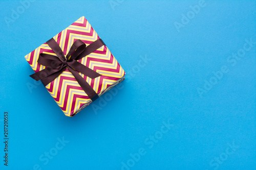 Hands holding wrapped gift box with colored ribbon as a present for Christmas, new year, mother's day, anniversary, birthday, party,  on blue background, top view. Present for a colleague at work.