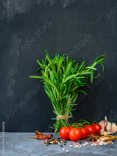 Rosemary, pepper, salt, tomatoes, garlic, anise. Herbs, spices and vegetables cooking on stone table. Dark concrete wall background with copyspace. photo