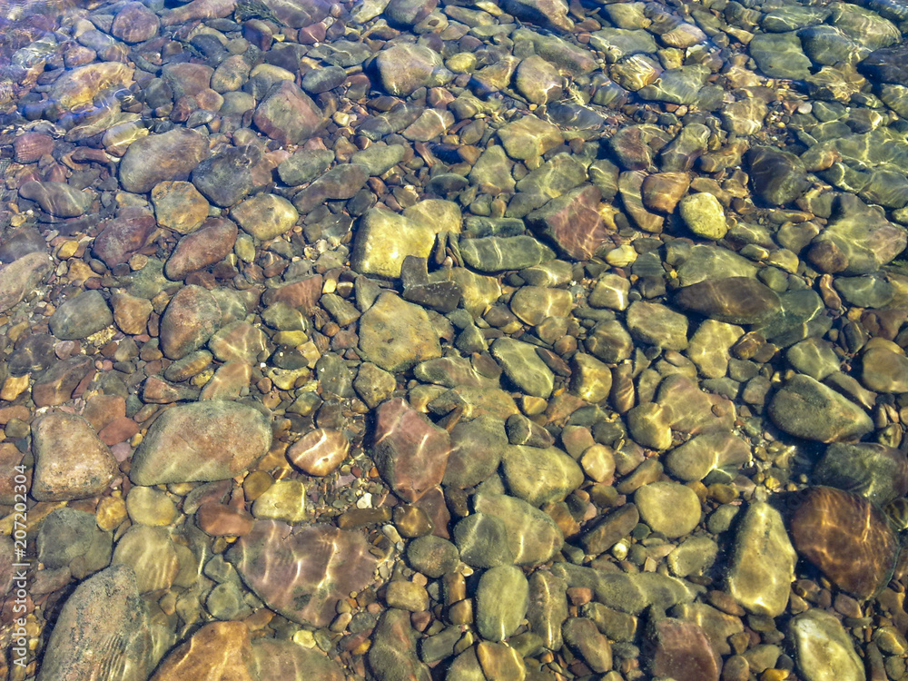 Clear water of a mountain river. Sun glare on river stones under clear water Clear water of a mountain river. Sun glare on river stones under clear water