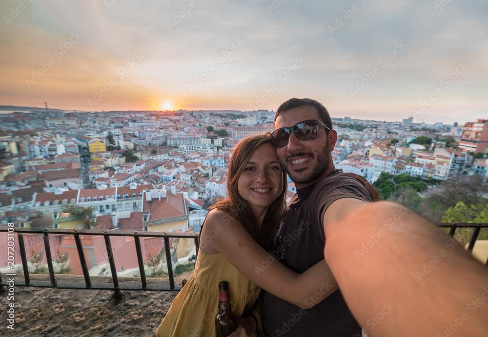 handsome tourists take selfie photo with view on Lisbon,Portugal from miradouro on sunny clear day holding portugal flag.Honeymoon loving romantic couple traveling to european city for holiday