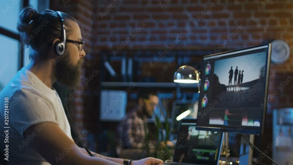 Side view of casual man in headphones working on computer and editing video with color correction