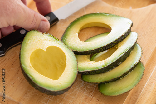 Male Hand Prepares Fresh Cut Avocado With Heart Shaped Pit Area On Wooden Cutting Board