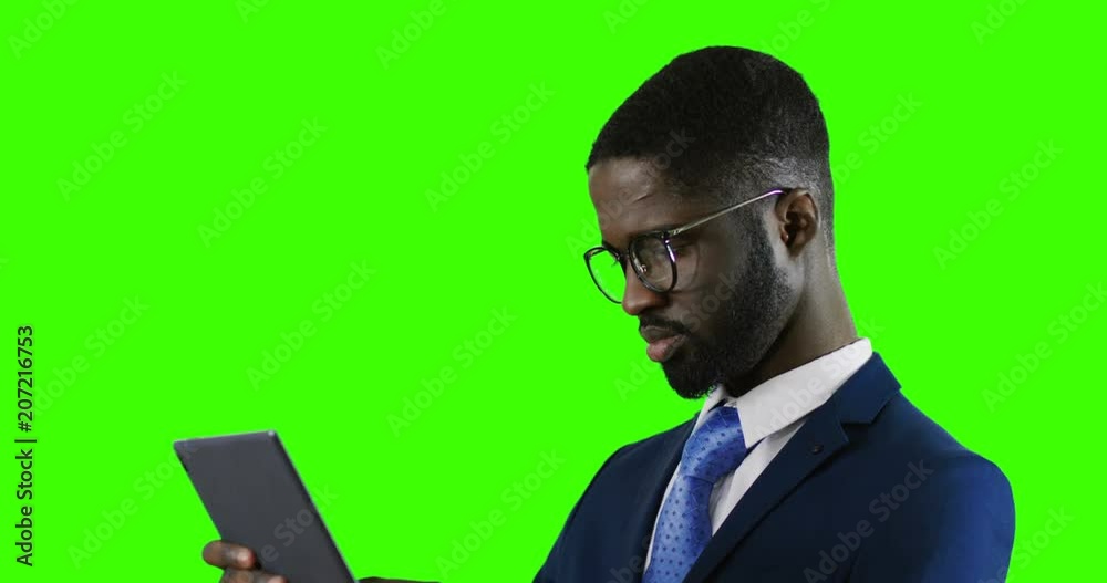 Close up of the African American businessman in glasses, suit and tie using tablet computer. Green screen background. Chroma key. Close up of the African American businessman in glasses, suit and tie using tablet computer. Green screen background. Chroma key.