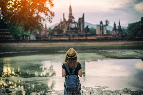 Young woman hipster backpacker traveling into Wat Mahathat temple in the Sukhothai Historical Park contains the ruins of old Sukhothai, Thailand, UNESCO world Heritage Site.