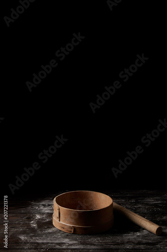 closeup shot of sieve and rolling pin on wooden table covering by flour isolated on black background