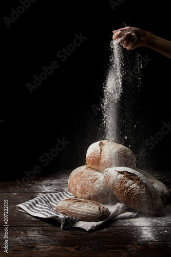 Fényképezés partial view of female baker sieving flour over various types of bread on sackcl
