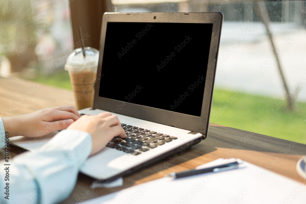 Close-up of business female working with Mockup image of laptop with blank black screen make a note in coffee shop like the background. - obrazy, fototapety, plakaty 