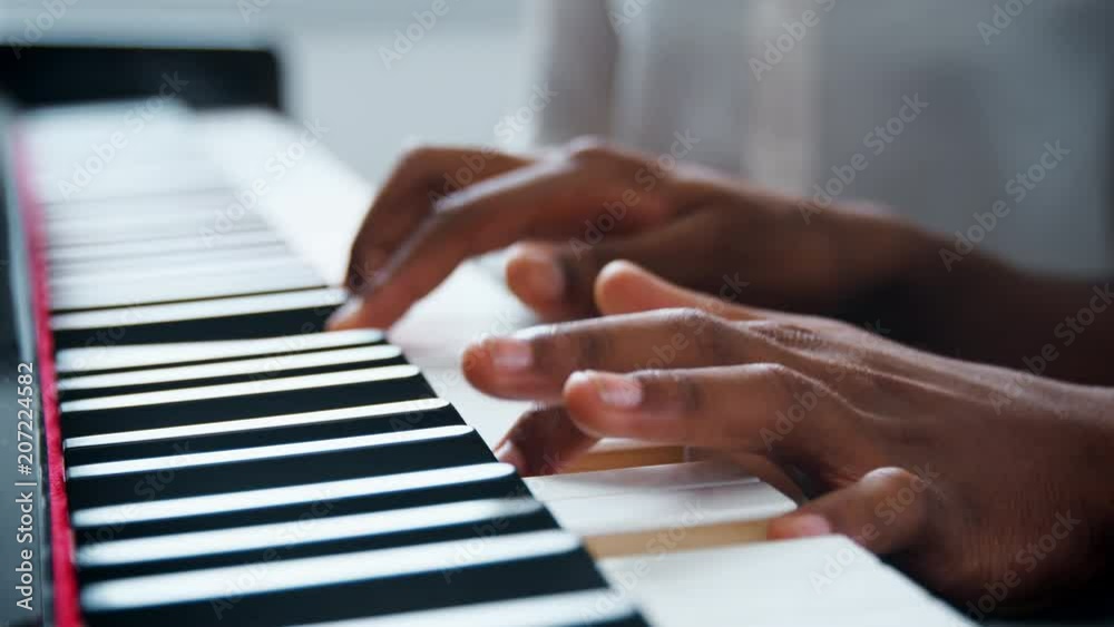 Close Up Of Pupil With Teacher Playing Piano In Music Lesson