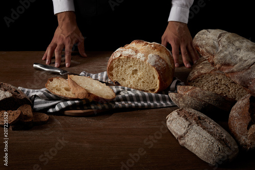 partial view of male baker standing near table with bread, knife and sackcloth