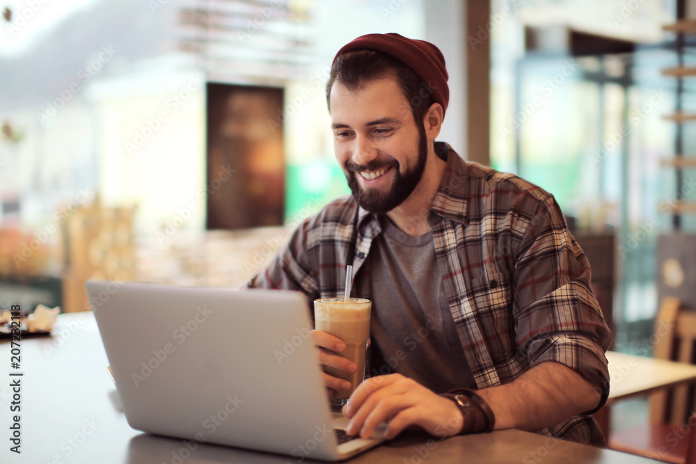 Handsome trendy hipster with glass of coffee drink using laptop in cafe Handsome trendy hipster with glass of coffee drink using laptop in cafe