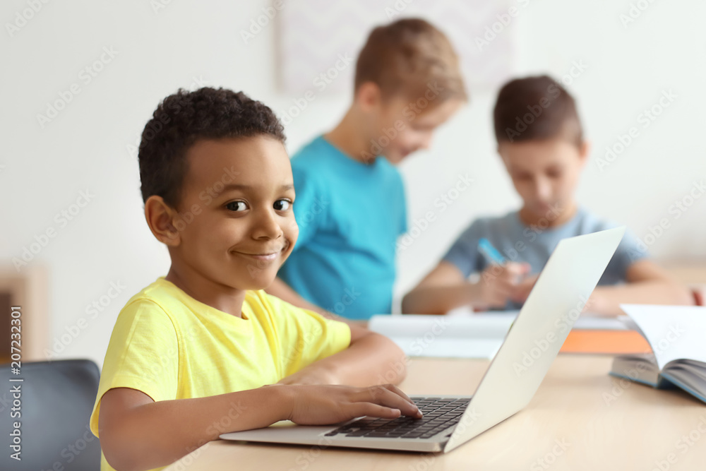 Cute African American boy with laptop doing homework in classroom at school Cute African American boy with laptop doing homework in classroom at school