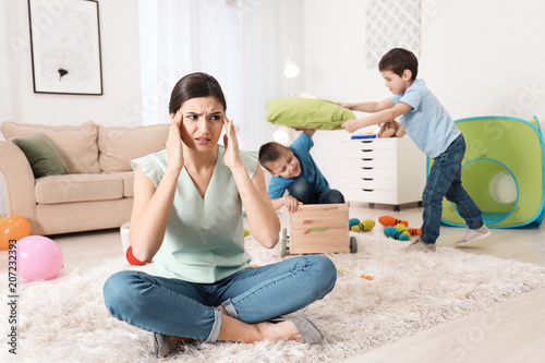 Tired young nanny and little boys playing in room