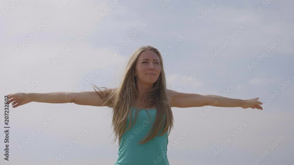 Young happy woman raising her hands up in slow motion. Happiness, freedom, power and motivation concept. Active and healthy lifestyle. Pretty smiling girl wearing sunglasses. Young happy woman raising her hands up in slow motion. Happiness, freedom, power and motivation concept. Active and healthy lifestyle. Pretty smiling girl wearing sunglasses.