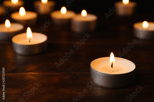 Wax candles burning on table in darkness, closeup