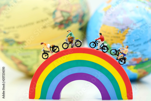 Miniature people : Travelers riding bicycle on rainbow with world map,travel concept.