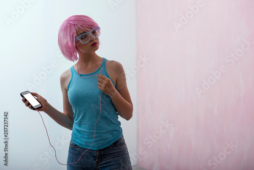 A young woman with a pink hair and neon glasses is using a smartphone.