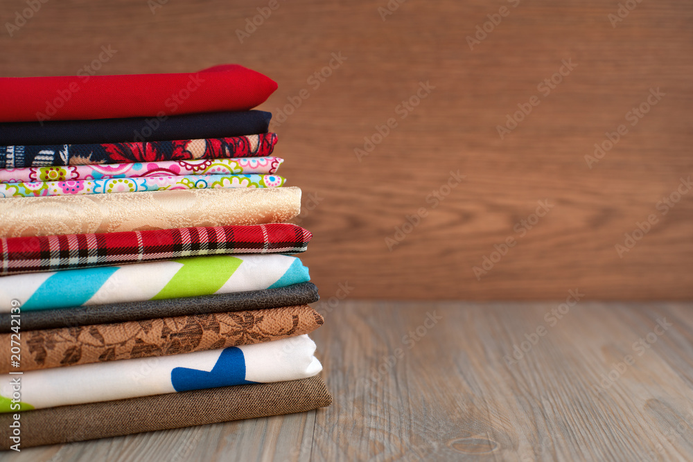 A stack of multi-colored fabric for sewing. Many different fabrics are  stacked on a table. Fabric for sewing clothes and bed linen. Stock Photo