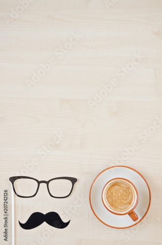 Mustache, glasses and cup of coffee on wooden background. Happy Father's day background