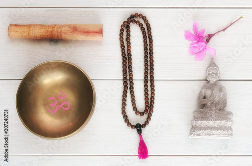 Essential accessory for mindfulness or meditation. Wooden mala beads, tibetan singing Bowl with symbol OM   and Buddha statue with flower on wooden background photo