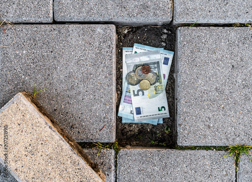 Euro banknotes and coins found under a loose pavement brick. Concept of running out of personal savings