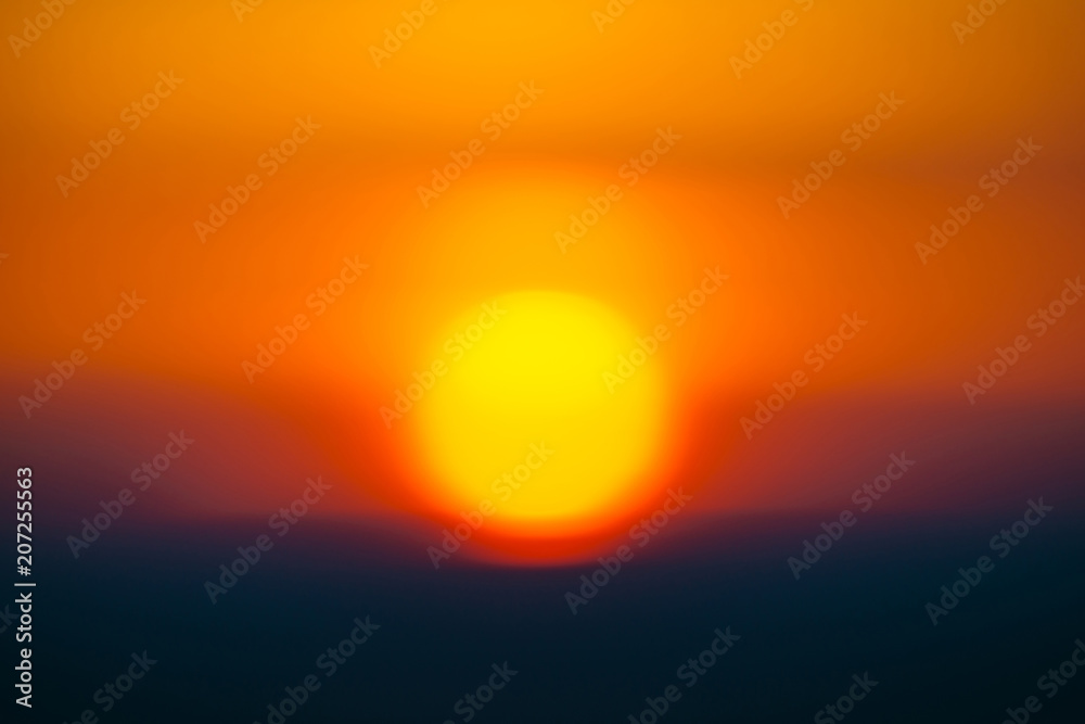 Blurry background image of circle of sun rising from behind dark horizon on background varicolored clouds of warmly shades. Abstract picturesque image of sun in bokeh in center. Blurry background image of circle of sun rising from behind dark horizon on background varicolored clouds of warmly shades. Abstract picturesque image of sun in bokeh in center.