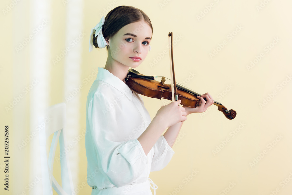 beautiful teenager in white outfit playing violin, isolated on yellow beautiful teenager in white outfit playing violin, isolated on yellow