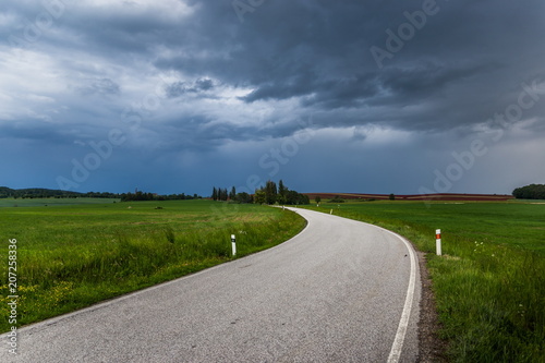 Dark stormy clouds over rural road at summer. Storm over countryside.