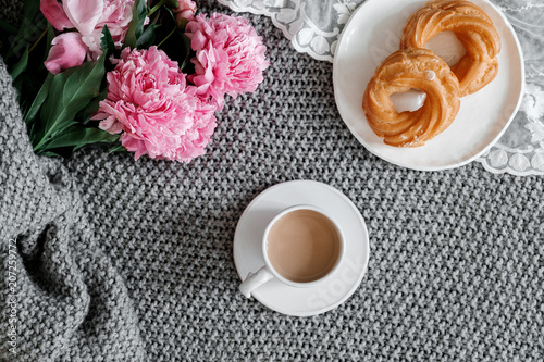 A cup of coffee with sweets and peonies on a gray background