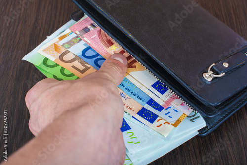 Male hand holding a leather wallet and withdrawing European currency Euro EUR